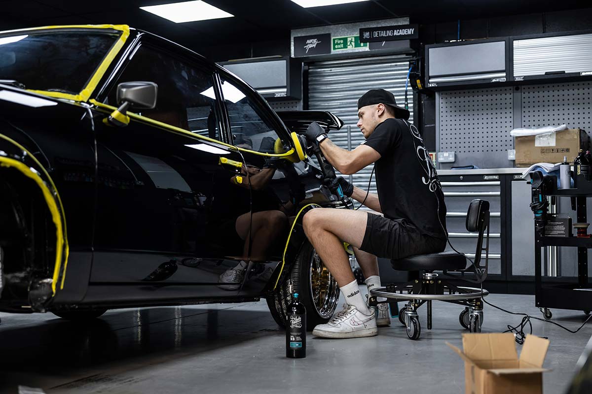 Mechanic working on a black car in a garage with tools and equipment around.