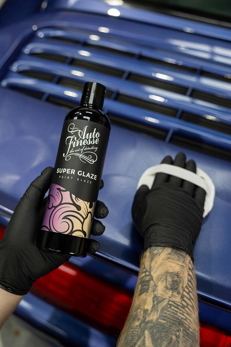 Person holding a bottle of Auto Finesse Super Glaze in front of a blue car.