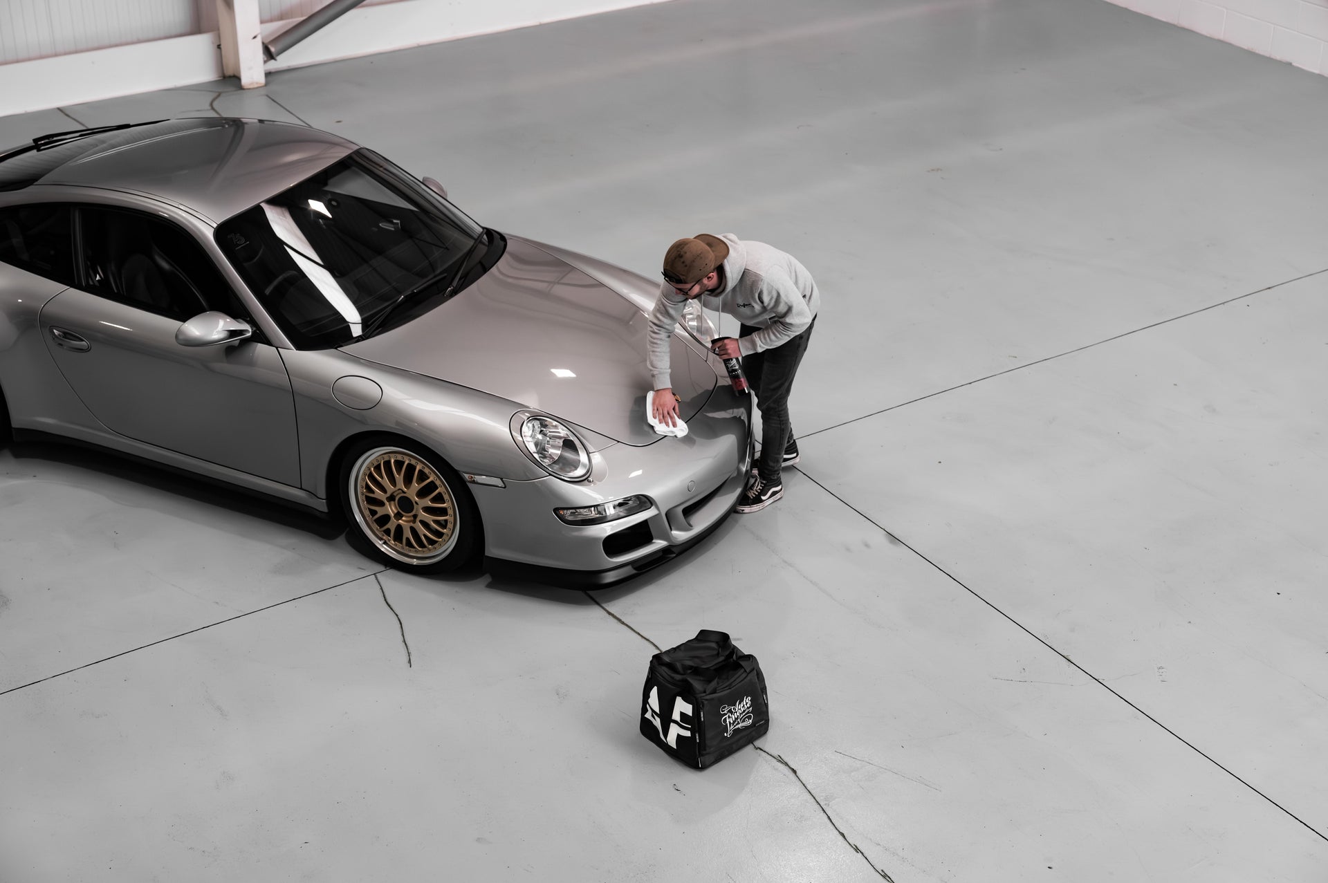 Person working on a silver Porsche car in a garage.