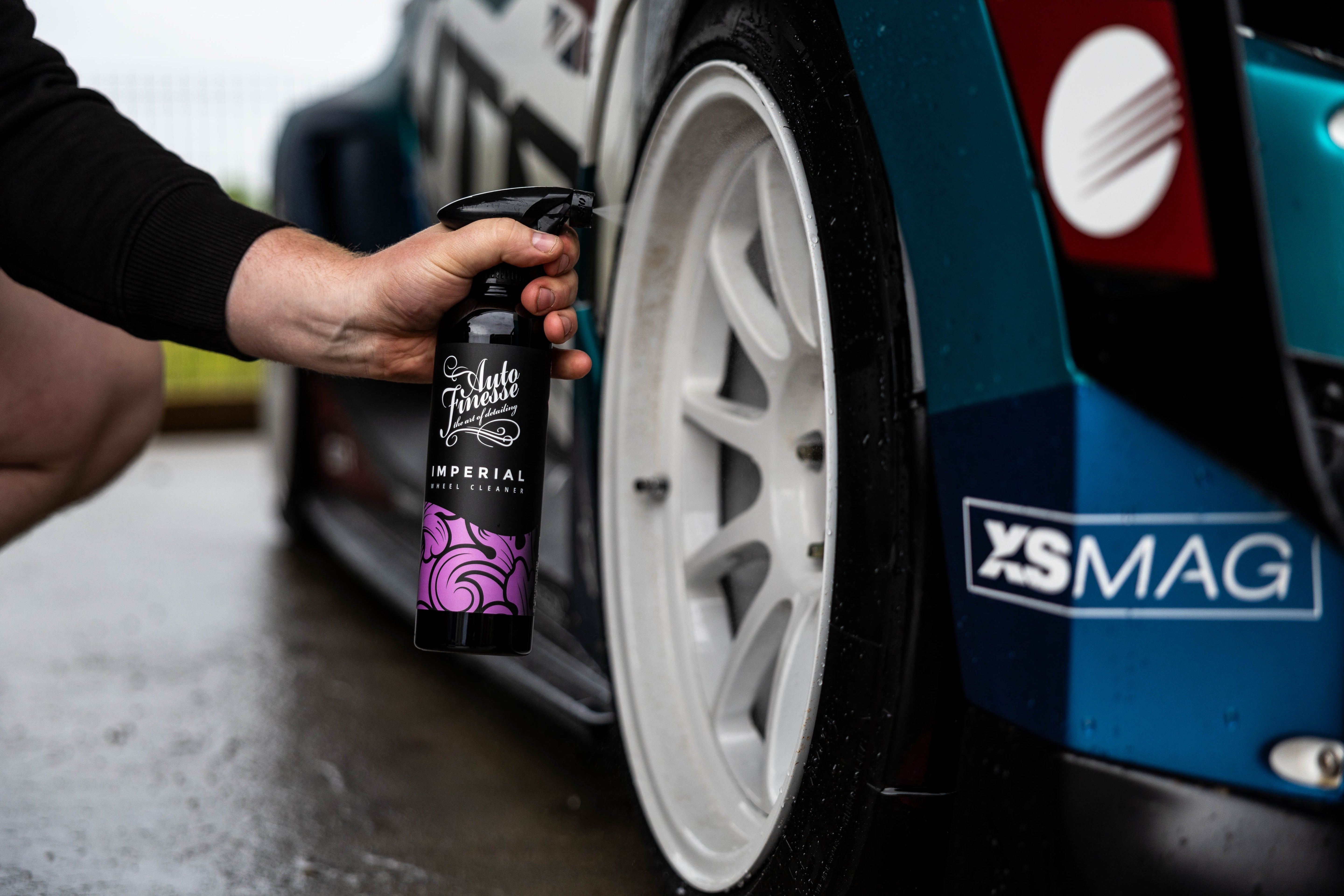 Person holding a spray bottle near a car wheel with 'XS MAG' branding.