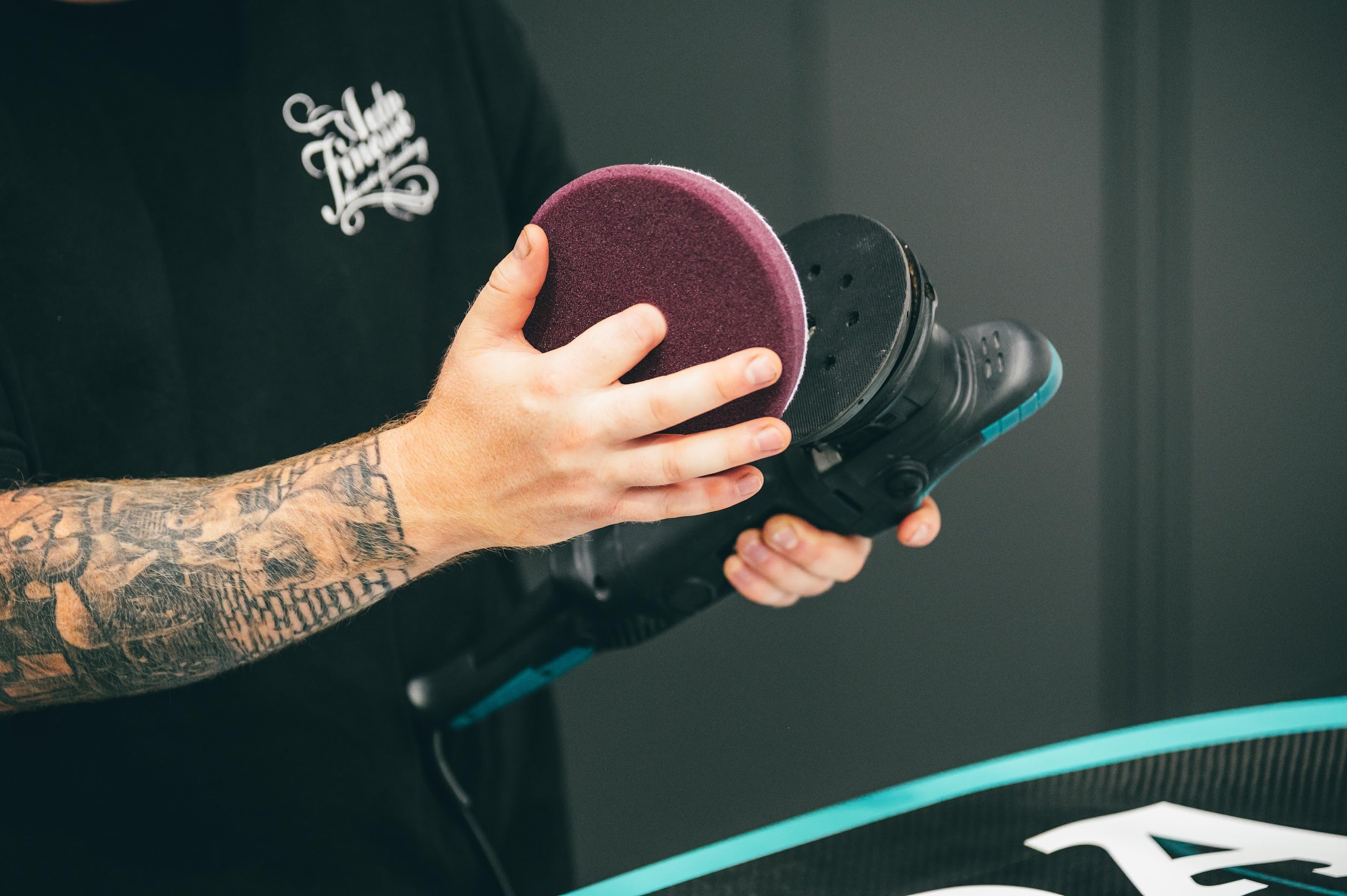 Person using a shoe polish machine with a purple pad on a dark background