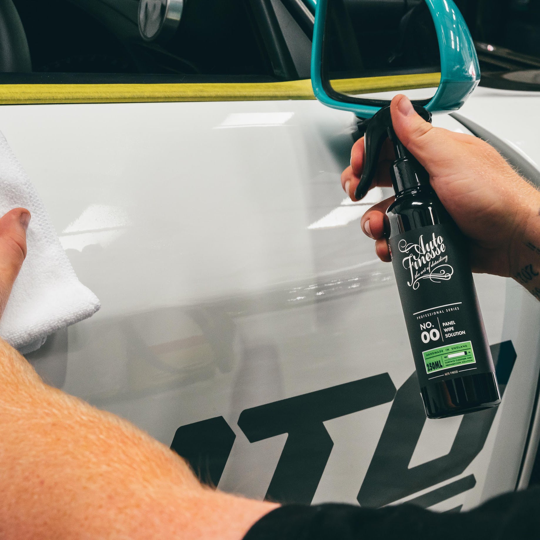Person cleaning a car window with a spray bottle labeled 'Lukoil' and a towel.