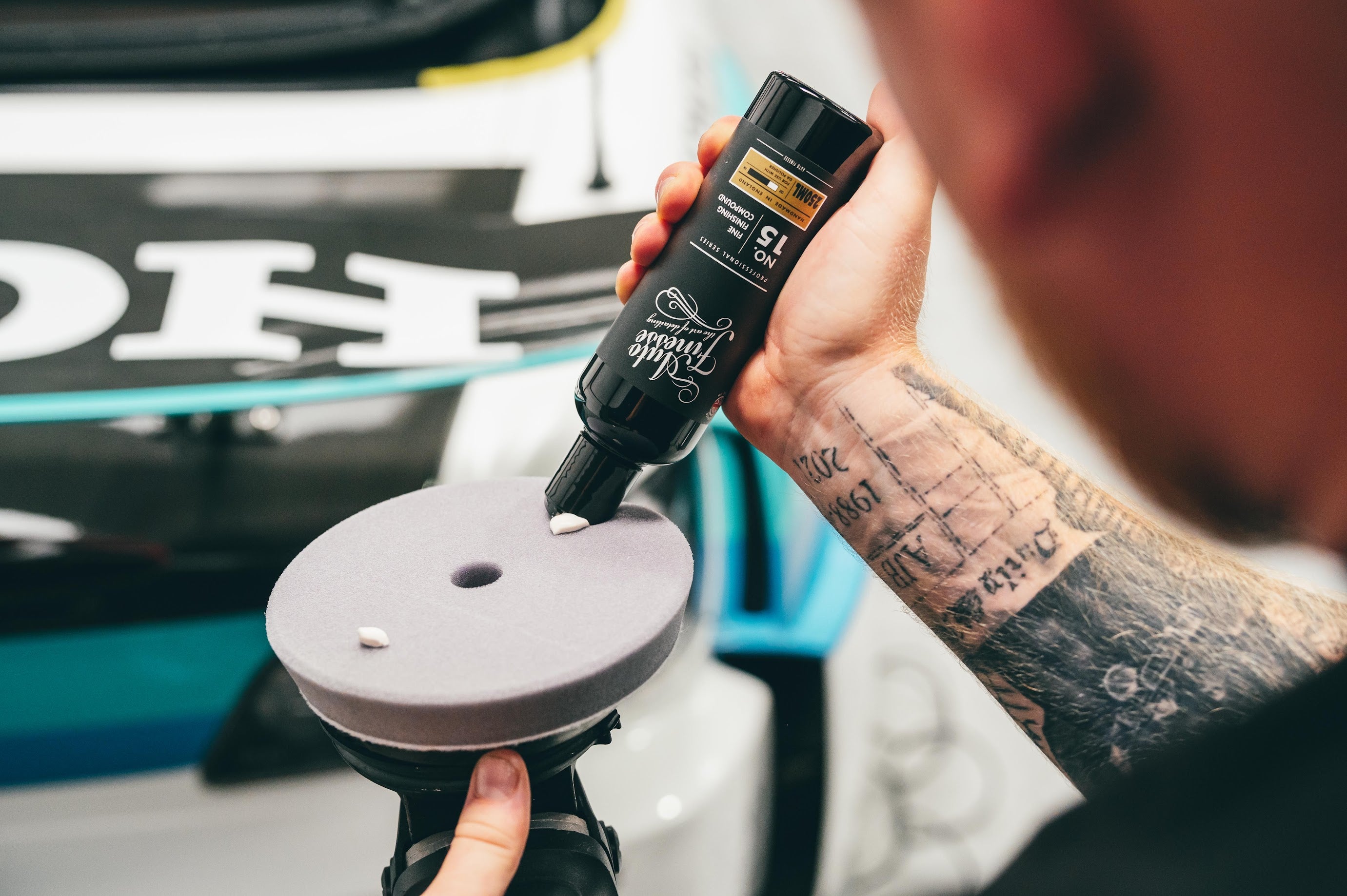 Person using a car detailing tool with a branded bottle in front of a car