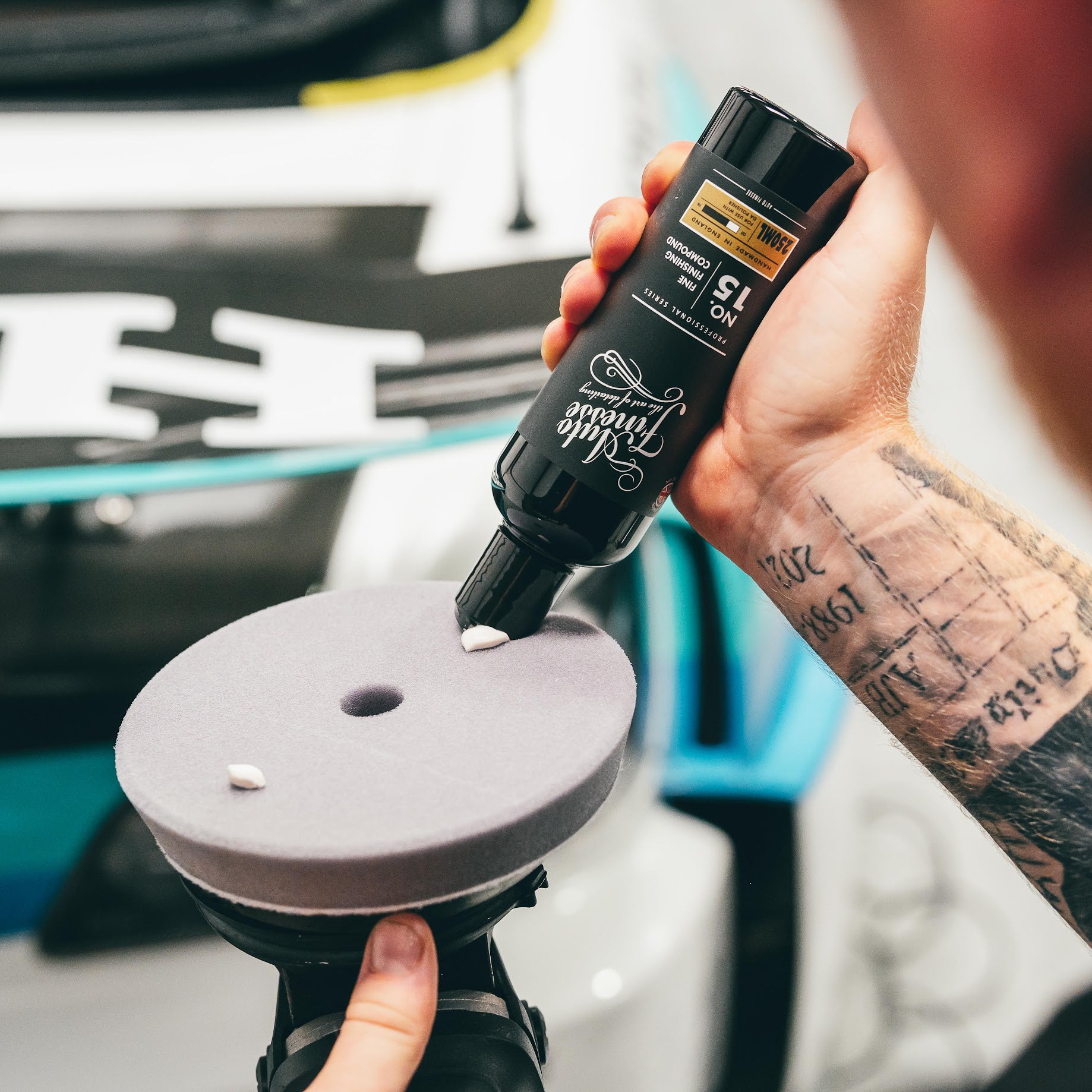 Person applying a product to a car polisher with a visible brand on the bottle.