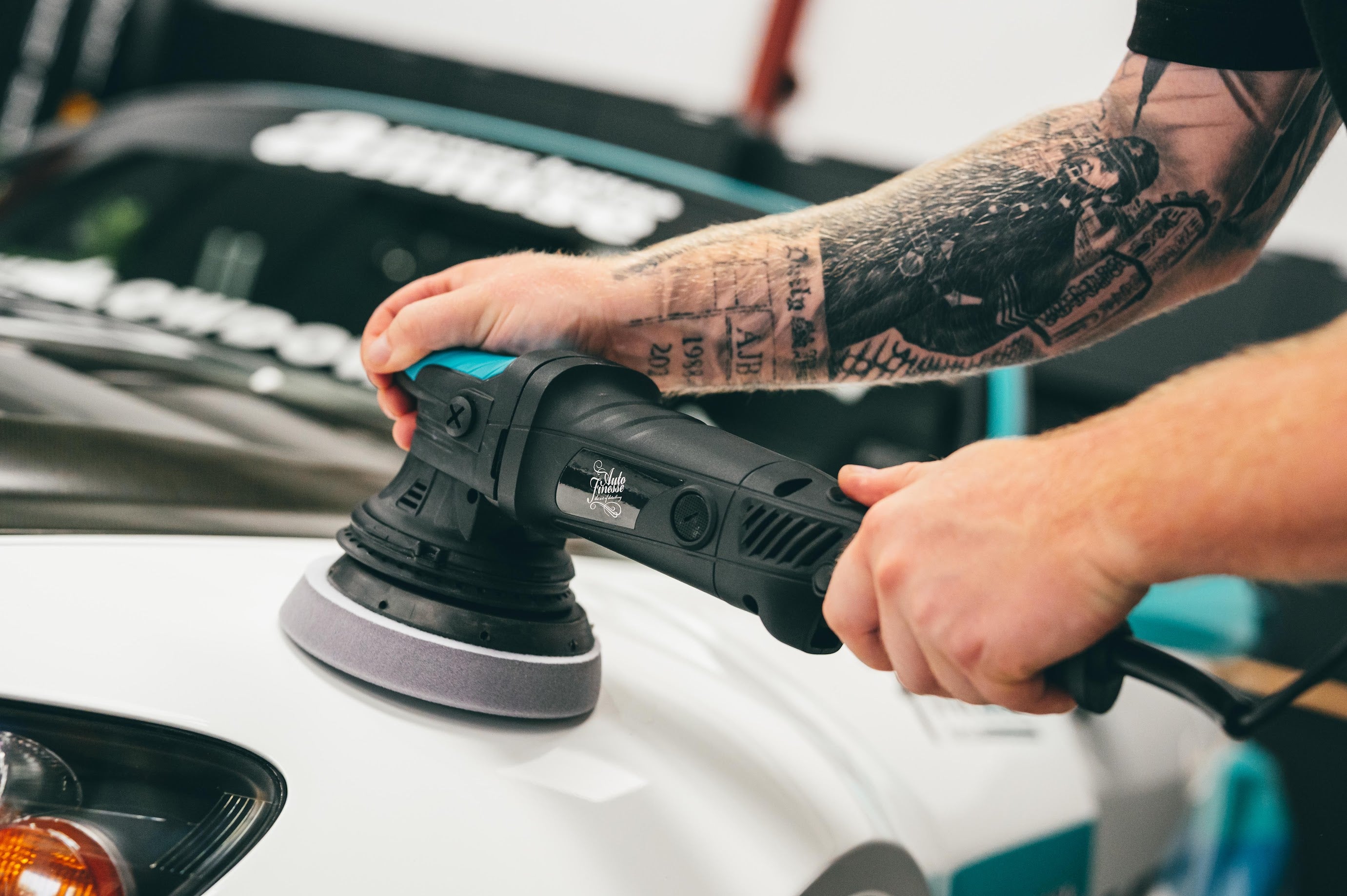 Person using a car polisher on a vehicle in a workshop setting