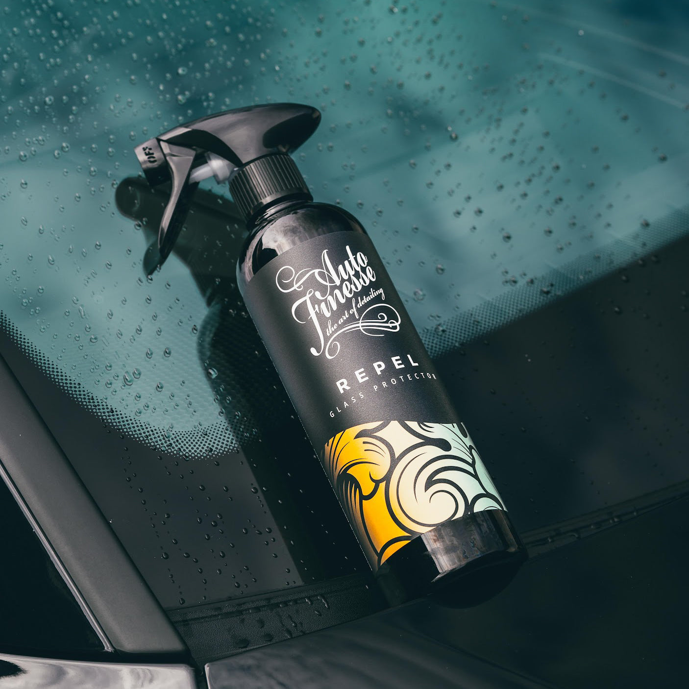 Spray bottle labeled 'Auto Finish' on a car window with water droplets.