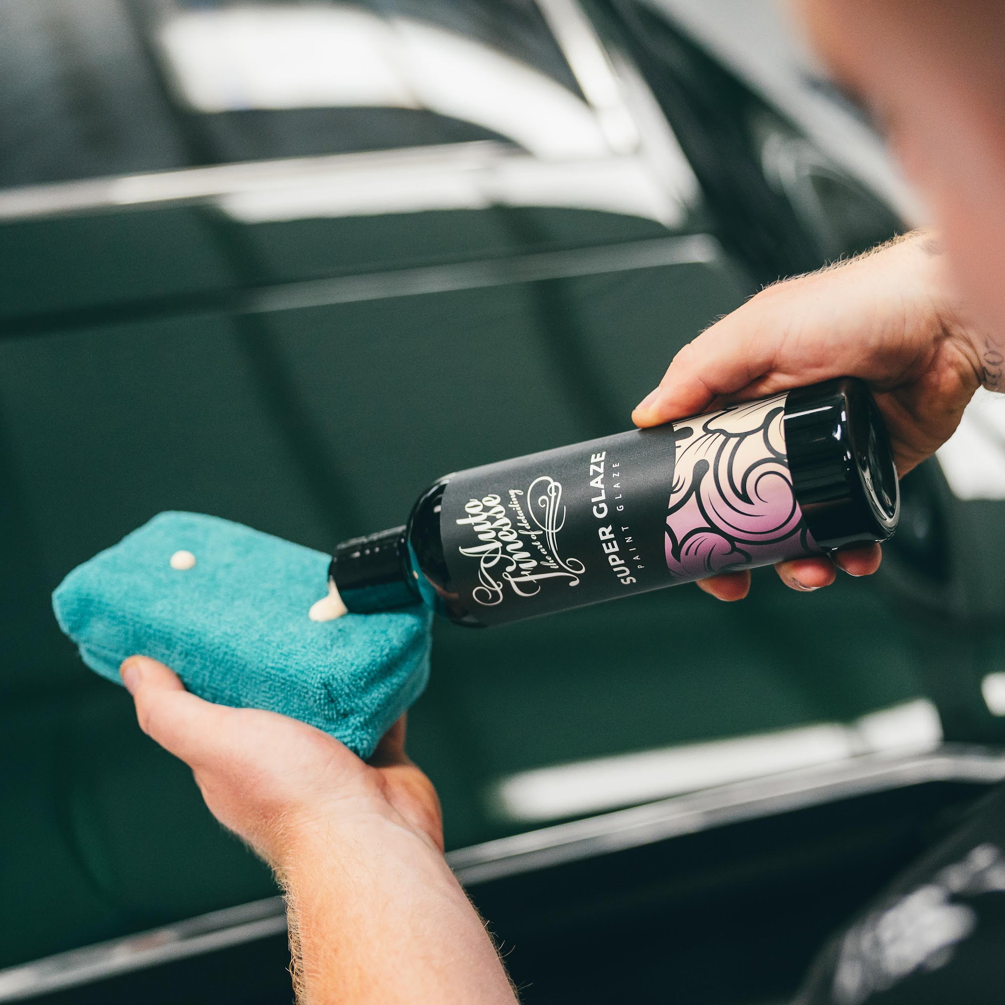 Person holding a car care product and a microfiber cloth in front of a car.