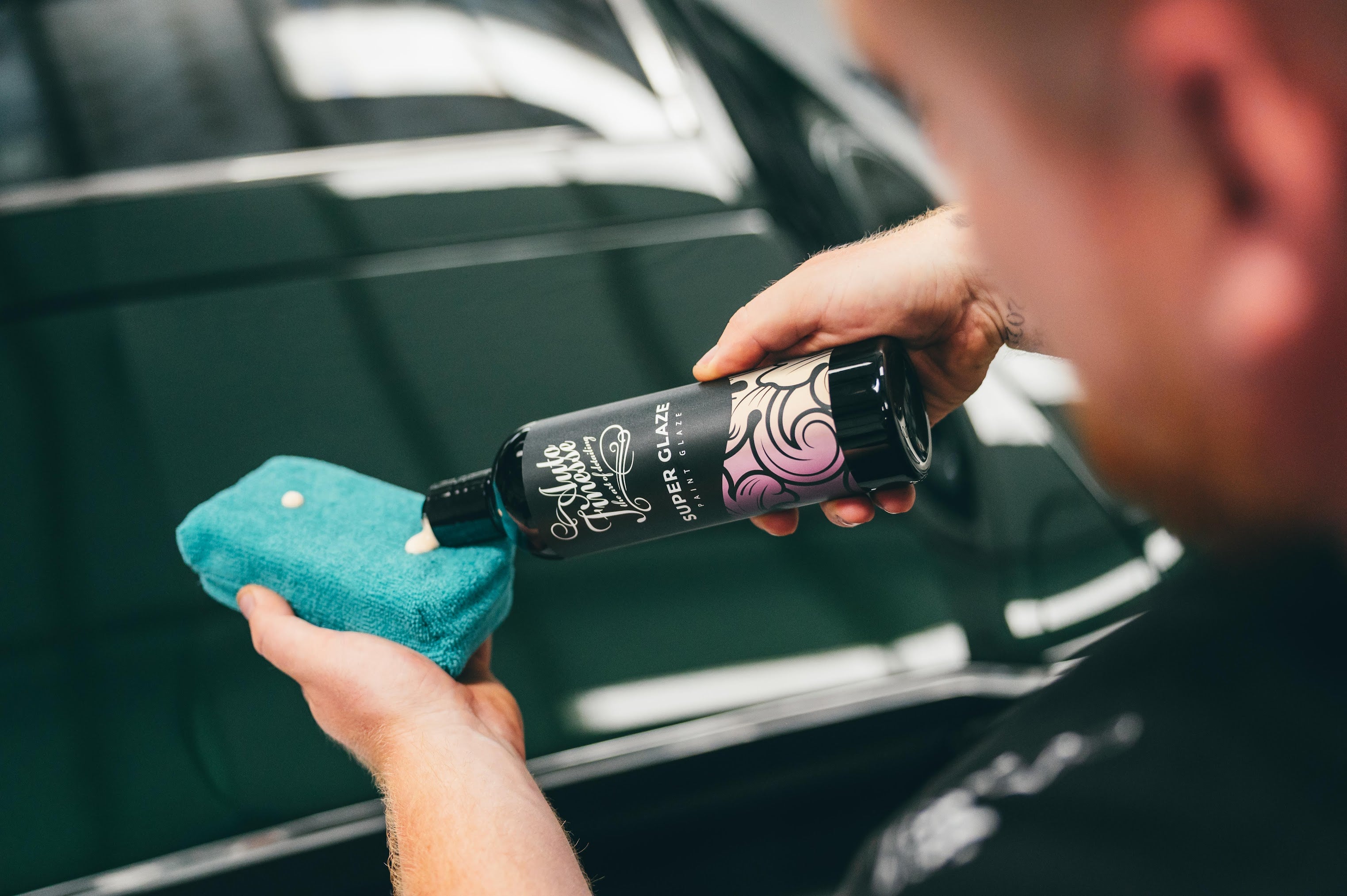 Person cleaning a car window with a cloth and a bottle labeled 'Muc-Off'.