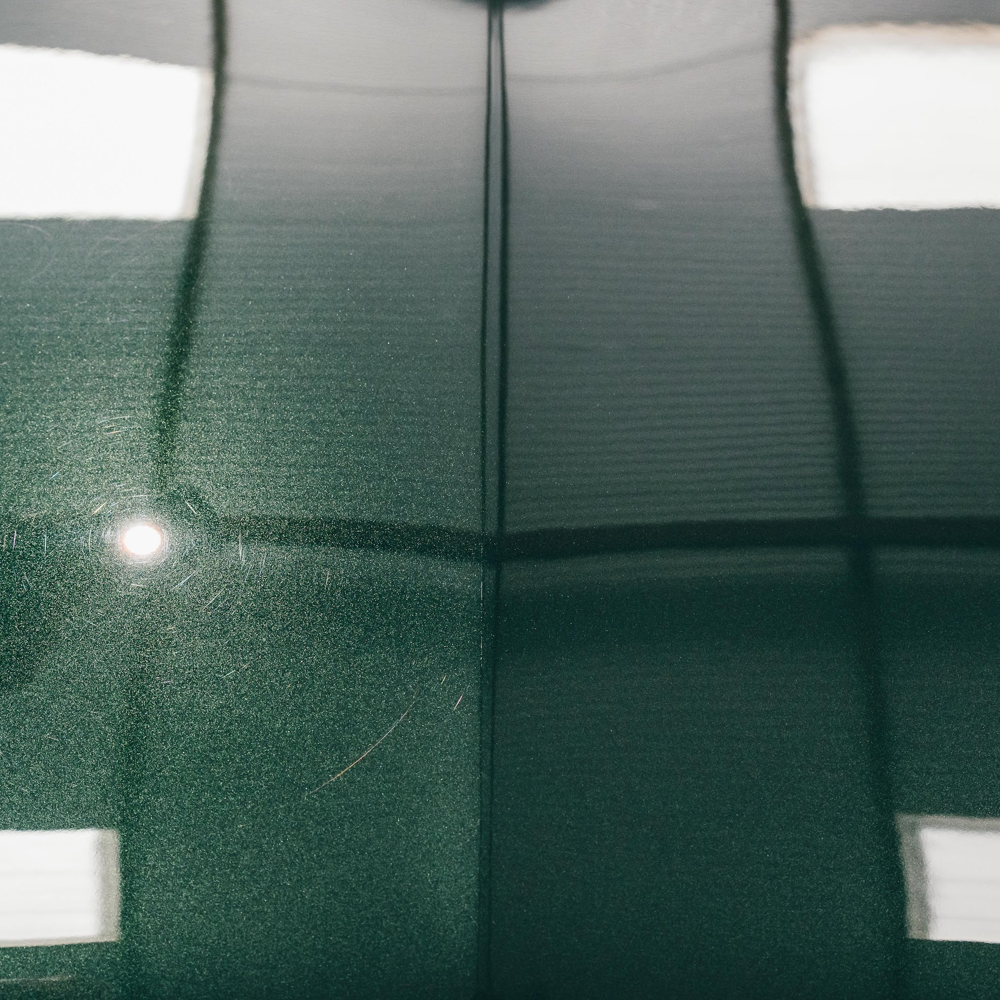 Close-up of a green car surface with visible scratches and reflections.