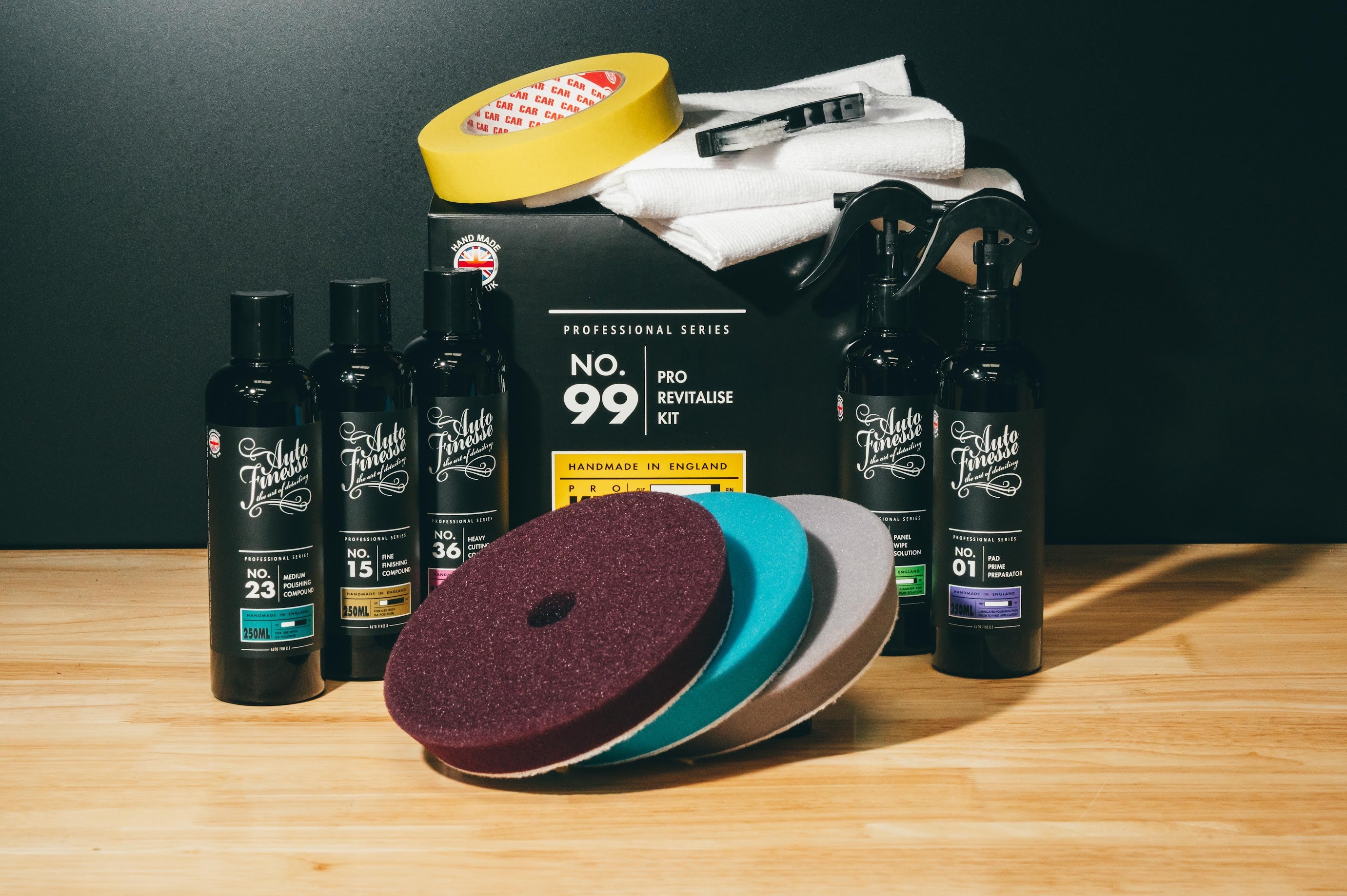 Car care products including bottles, a box, and sanding discs on a wooden surface with a dark background.