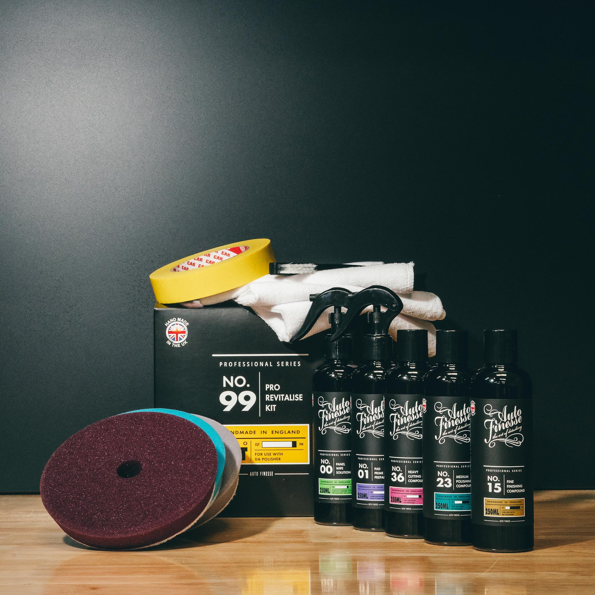 Collection of car care products including bottles, a sanding disc, and a box on a wooden surface with a dark background.