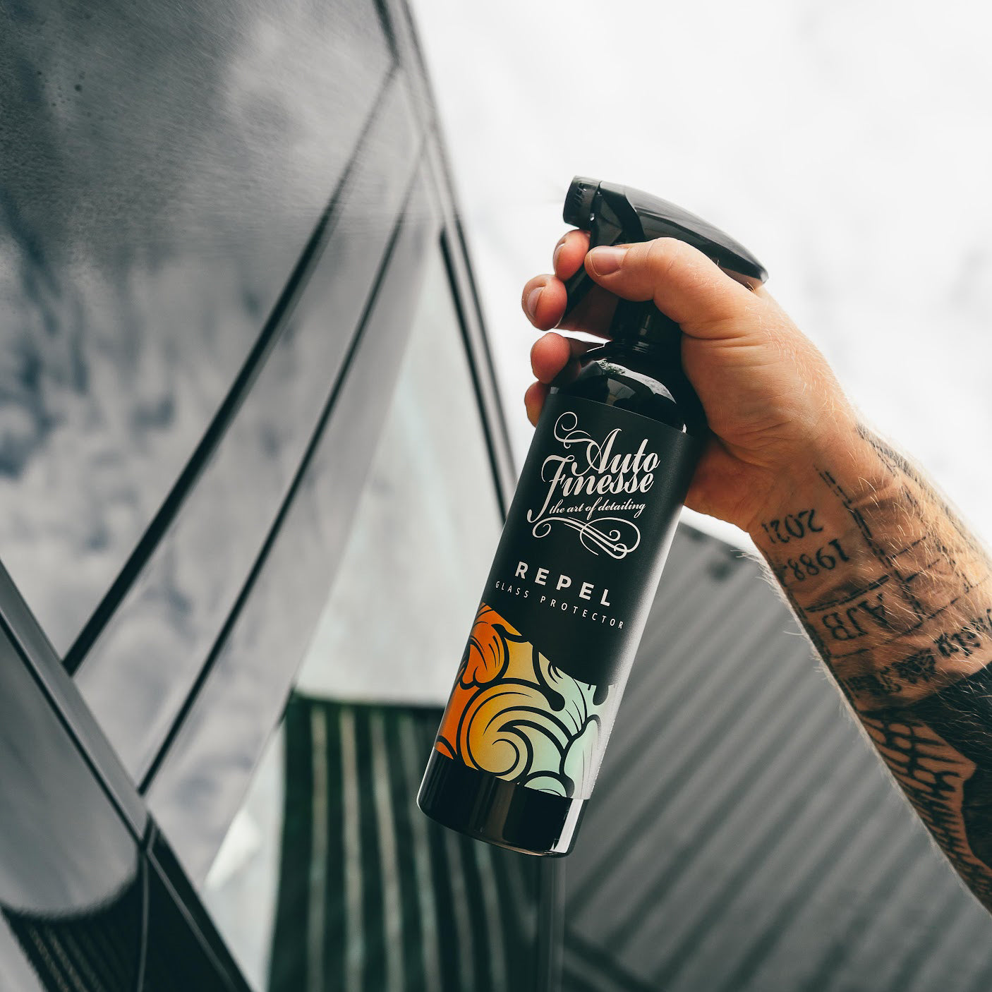 Hand holding a bottle of Auto Finesse Repel glass protection spray against a blurred background.