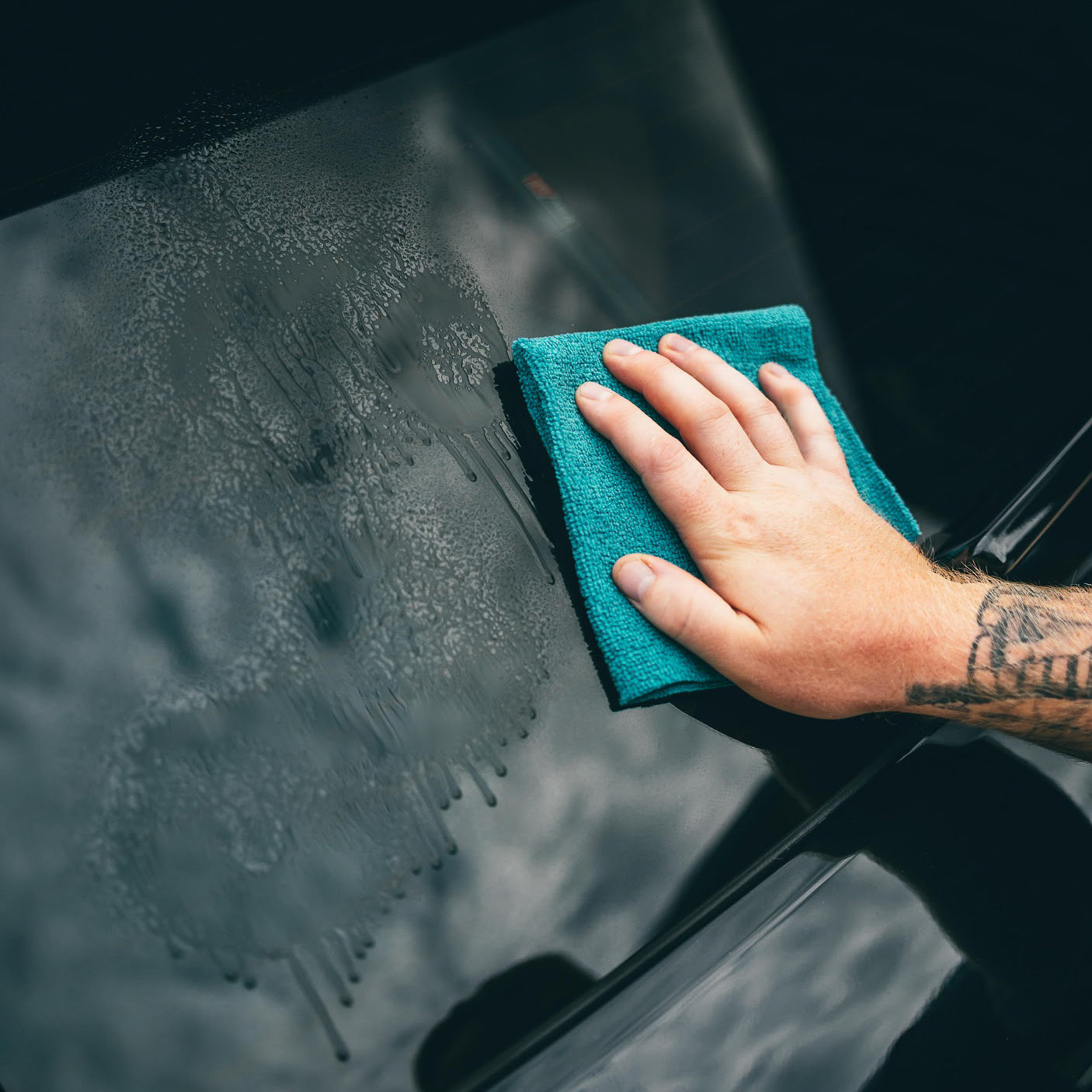 Hand cleaning a car window with a blue microfiber cloth